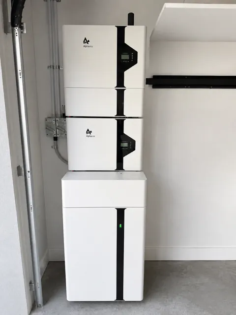 Stacked home battery with its inverter mounted above it inside a garage