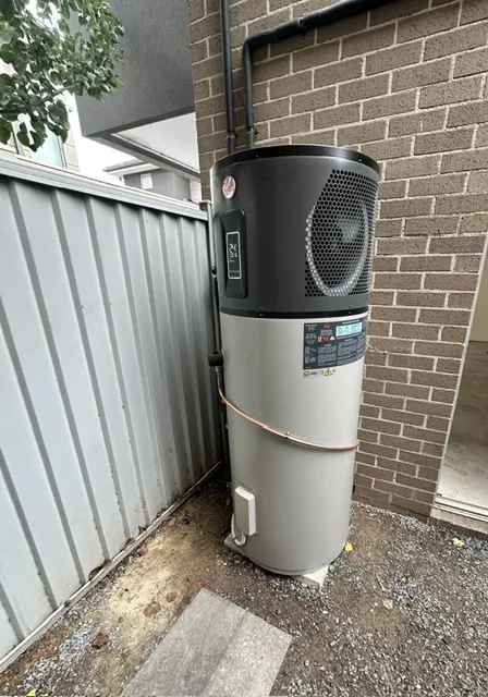Electric heat pump hot water unit installed beside a colorbond fence