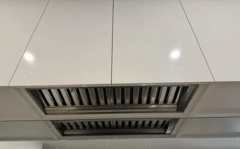 Stainless steel undermount rangehood fitted beneath white overhead kitchen cabinets