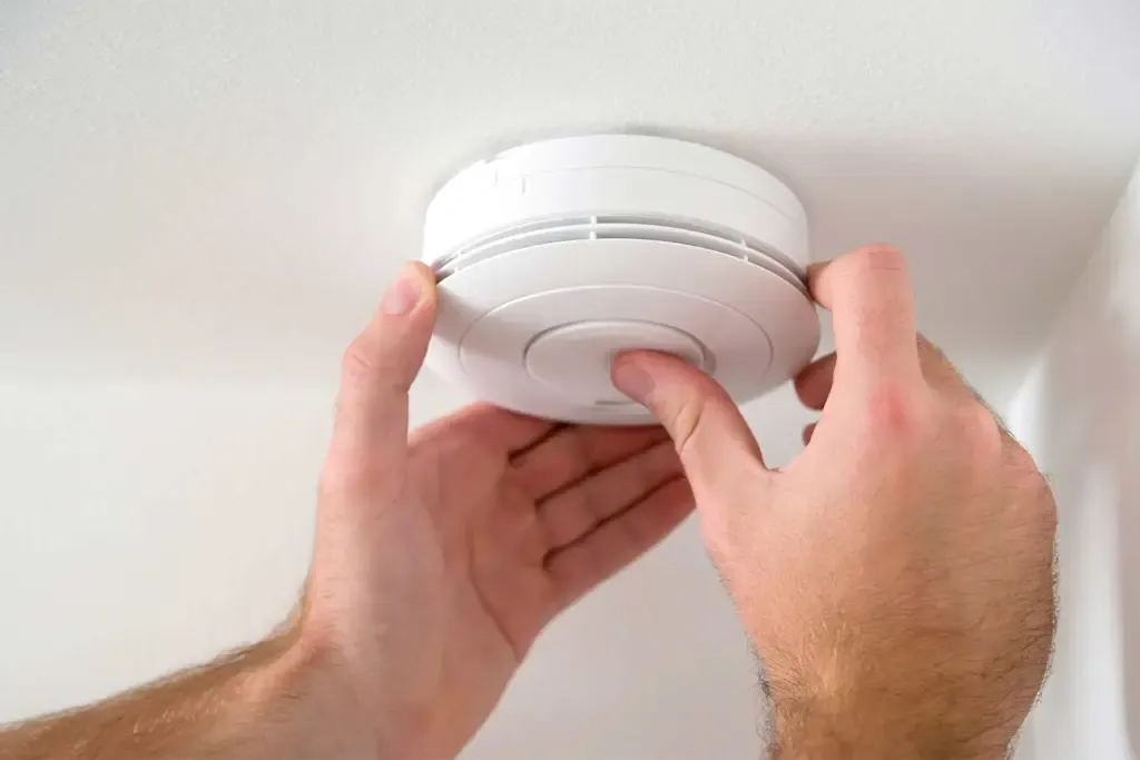 Hands fitting a photoelectric smoke alarm to a ceiling mount