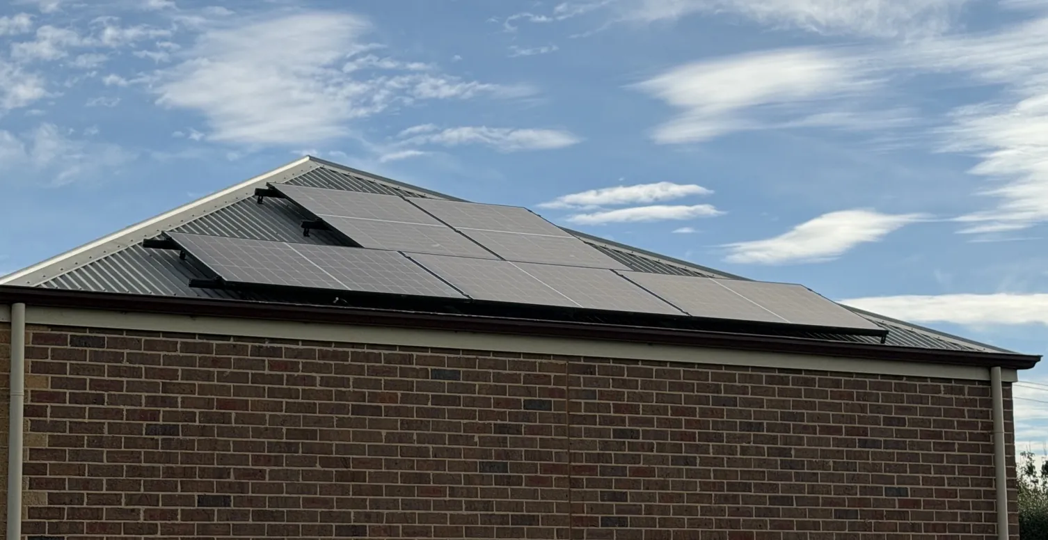 Solar panels along the roof of a brick home under a blue sky