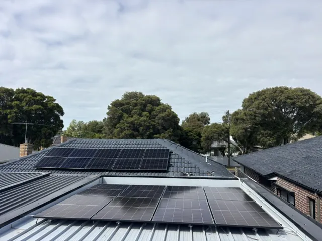 Rows of solar panels along a suburban roof with trees behind