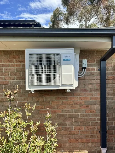 Fujitsu split system outdoor unit mounted on a brick wall under the eaves